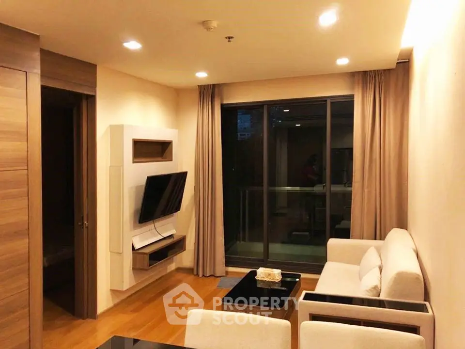 Modern living room with sleek furniture and large window leading to a balcony.
