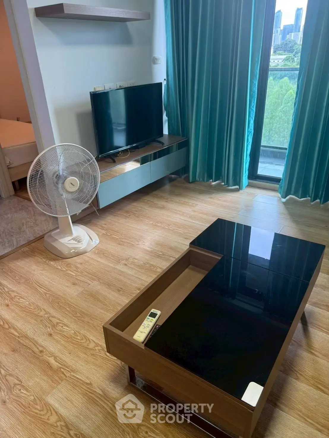 Modern living room with TV, fan, and glass coffee table overlooking city view.