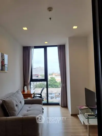 Modern living room with large window and city view, featuring a cozy sofa and sleek decor.