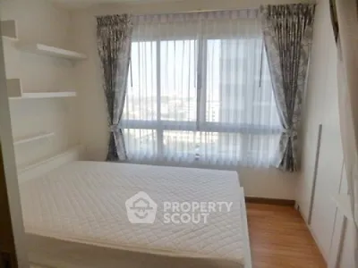 Bright bedroom with large window and elegant curtains, featuring a comfortable bed and wooden flooring.
