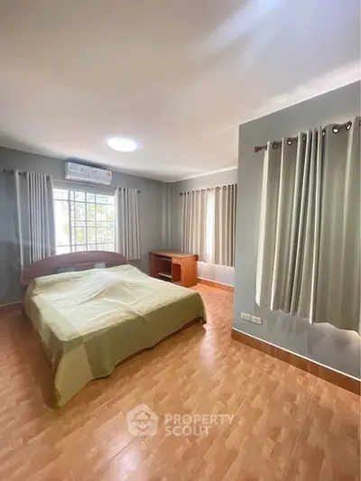 Spacious bedroom with large windows and natural light, featuring a cozy bed and wooden flooring.