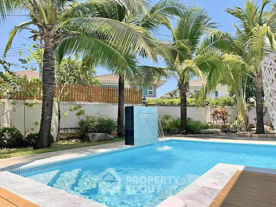 Luxurious backyard pool with palm trees and waterfall feature in tropical setting.