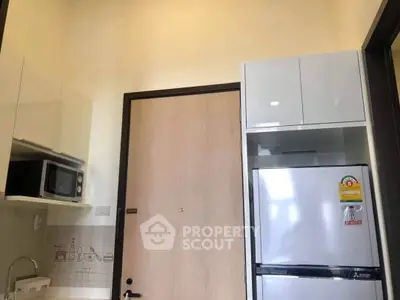 Modern kitchen with sleek cabinets, microwave, and refrigerator in a stylish apartment.