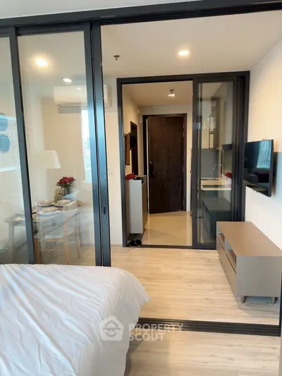Modern studio apartment with glass partition, cozy bedroom, and sleek kitchen design.