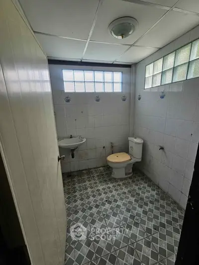 Compact bathroom with tiled walls and floor, featuring a toilet and sink under natural light.