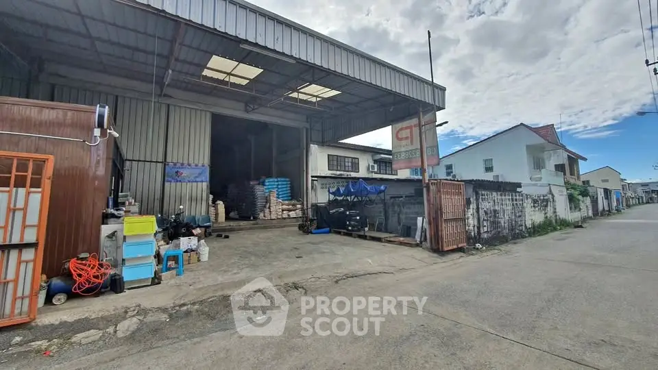 Spacious warehouse with open entrance and adjacent residential buildings, ideal for storage or commercial use.