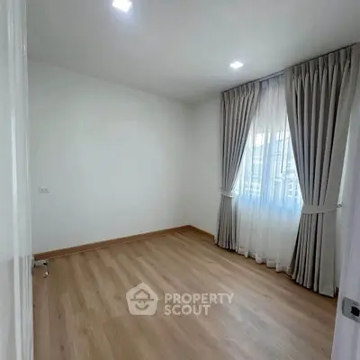 Spacious empty room with wooden flooring and large window, perfect for customization.
