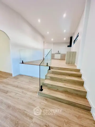 Modern open-plan living space with sleek wooden flooring and glass railing staircase.