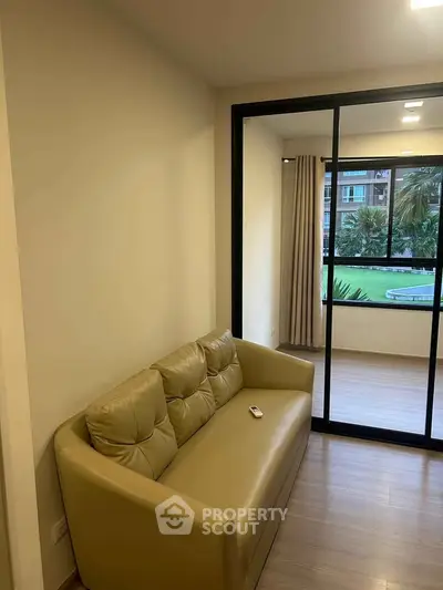 Modern living room with beige sofa and glass sliding doors leading to a bright balcony view.