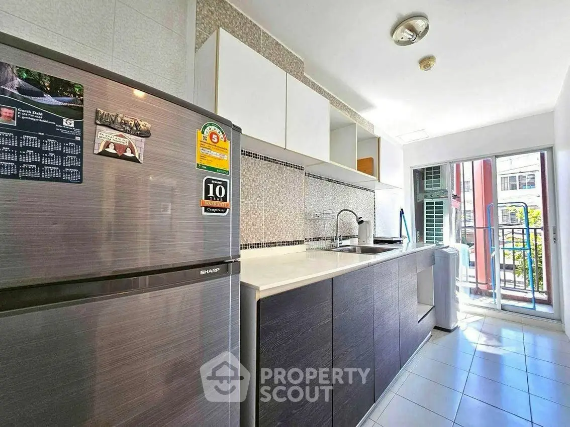 Modern kitchen with sleek cabinets, stainless steel fridge, and washing machine near balcony.