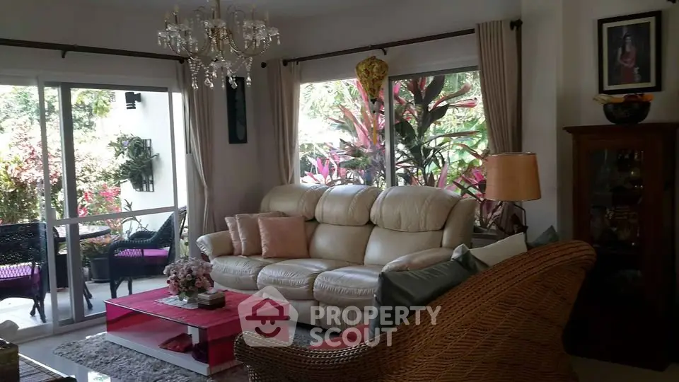 Charming living room with elegant chandelier and garden view, featuring cozy seating and vibrant decor.