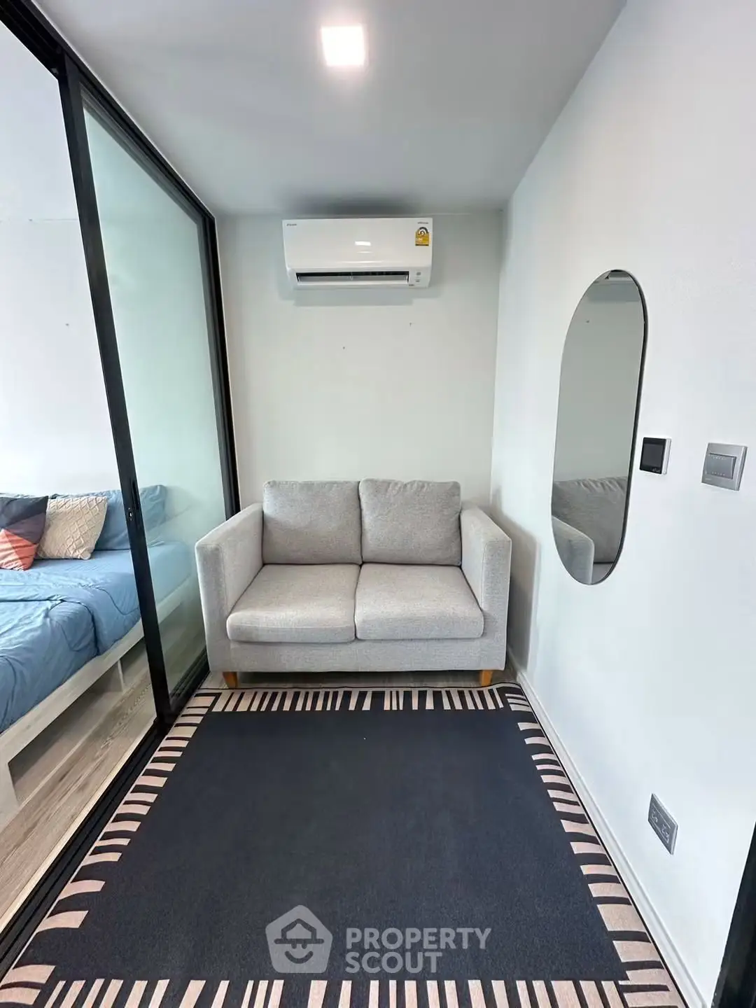 Modern compact living space with cozy sofa and stylish decor, featuring a glass partition and air conditioning.