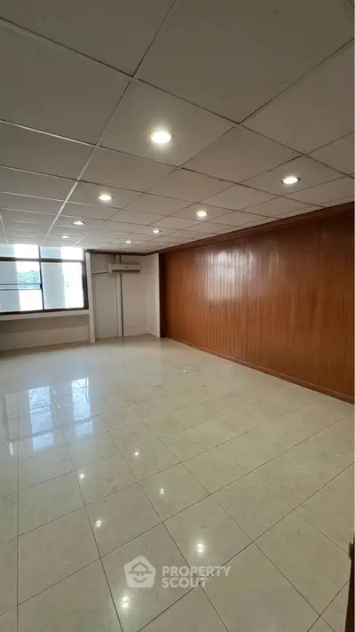Spacious empty room with tiled flooring and wood panel accent wall