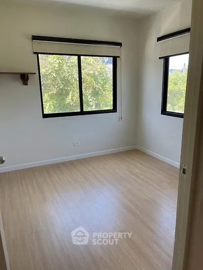 Bright empty bedroom with large windows and wooden flooring, perfect for customization.
