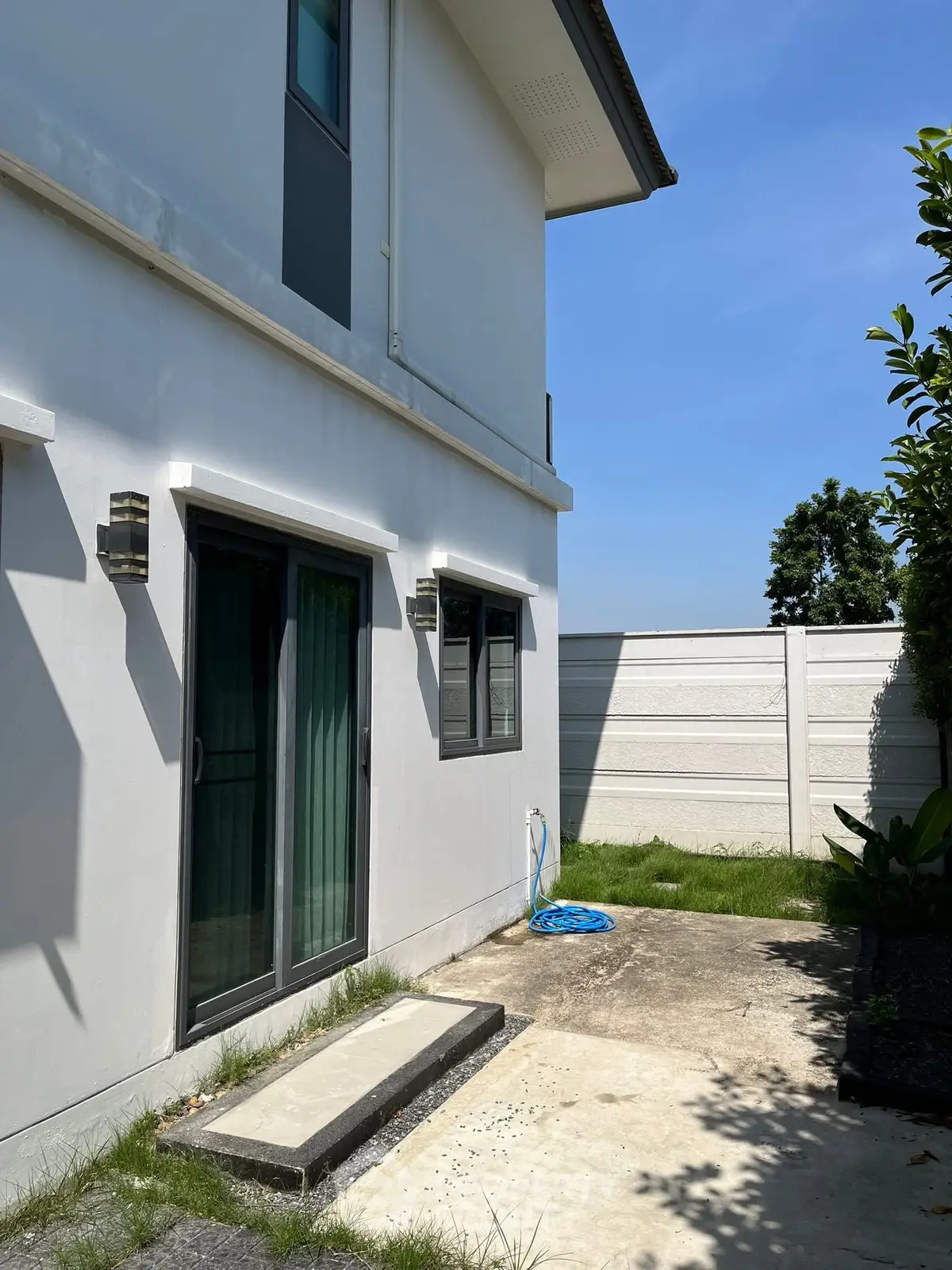 Modern two-story house exterior with sliding glass doors and lush green lawn under clear blue sky.