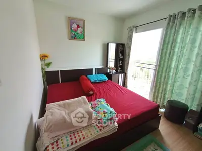 Cozy bedroom with red bedding, large window, and floral decor for a serene living experience.