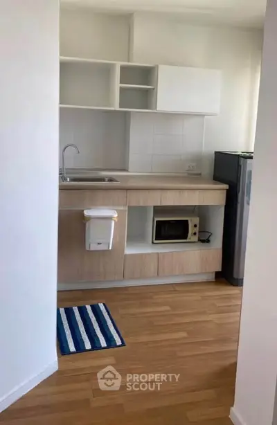 Modern compact kitchen with wooden cabinets and sleek appliances in a cozy apartment.