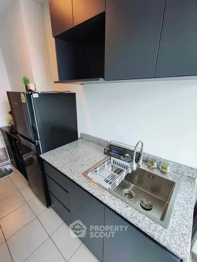 Modern kitchen with sleek black cabinets and granite countertops, featuring a stainless steel sink and refrigerator.
