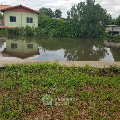 Scenic view of a serene pond with lush greenery and residential buildings reflecting in the water.