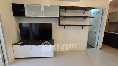 Modern living room with sleek TV unit and open shelving, adjacent to a stylish kitchen.