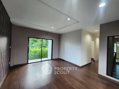Spacious living room with wooden flooring and large balcony access.