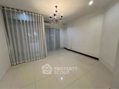 Spacious empty living room with elegant chandelier and large windows.