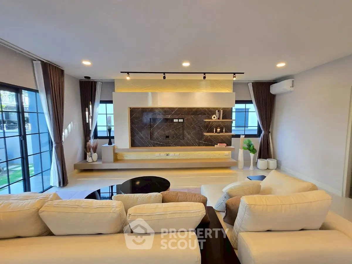 Modern living room with stylish decor and large windows, featuring a cozy seating area and elegant lighting.