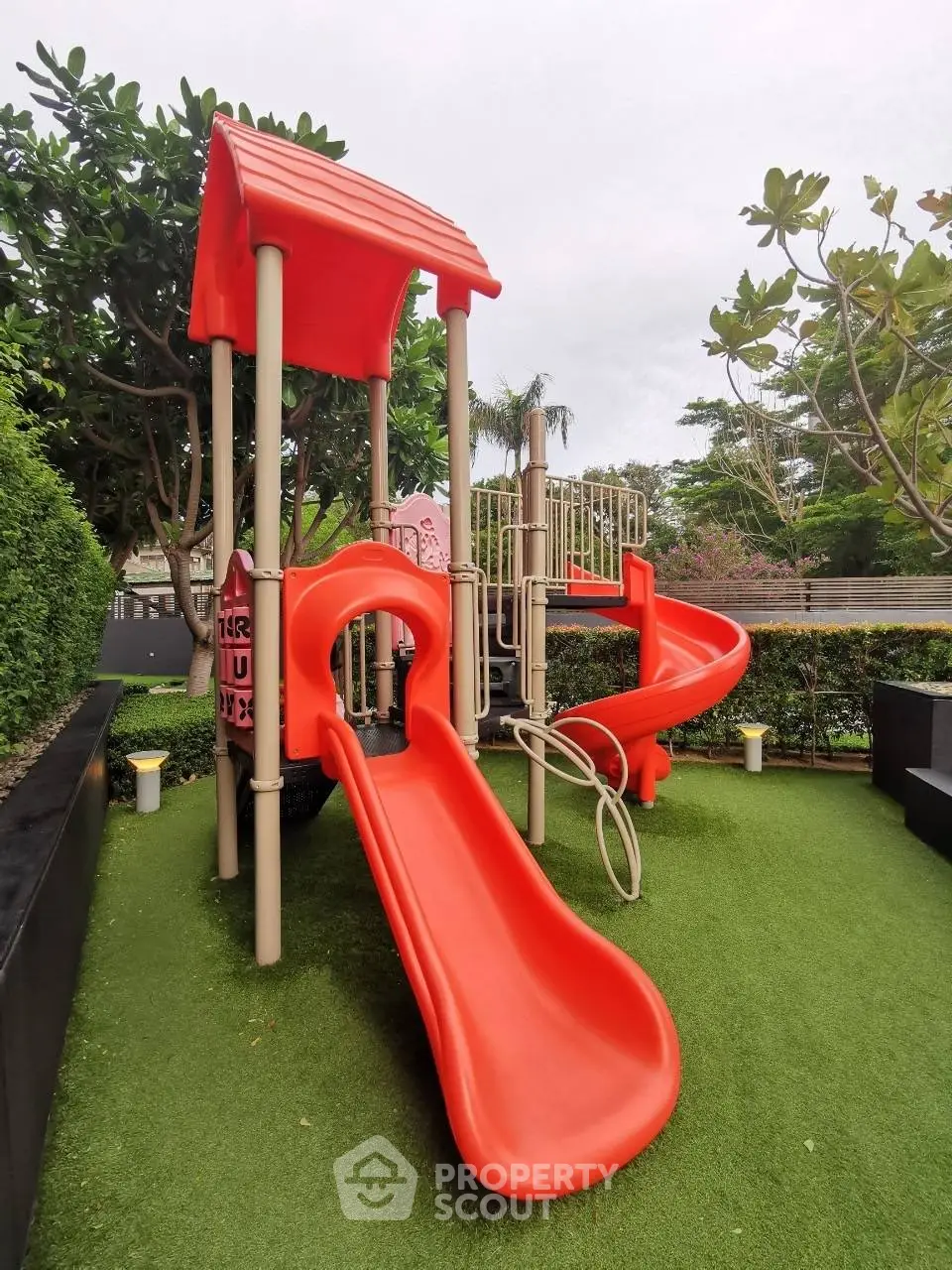 Charming outdoor playground with vibrant red slides and lush greenery, perfect for family-friendly real estate.
