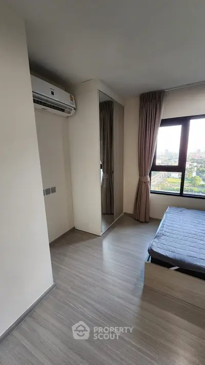 Modern bedroom with large window and mirrored closet, offering a bright and airy atmosphere.