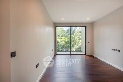 Spacious empty room with large window and wooden flooring, overlooking lush greenery.