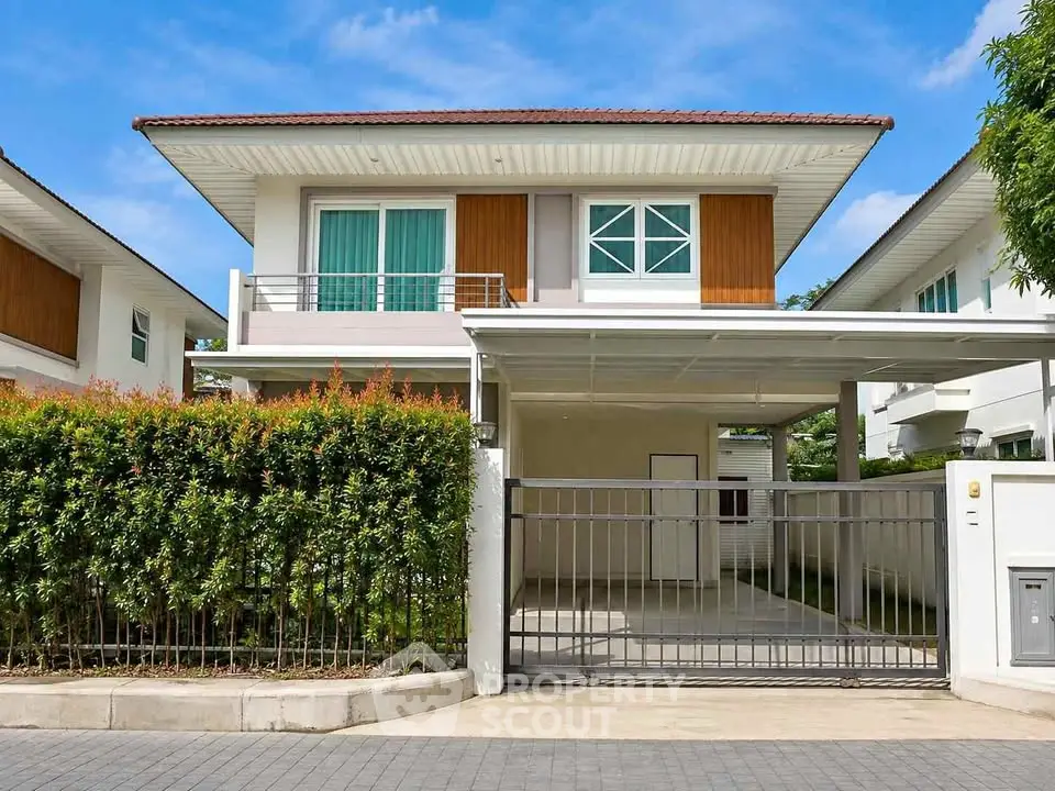 Modern two-story house with a gated driveway and lush greenery in a suburban neighborhood.