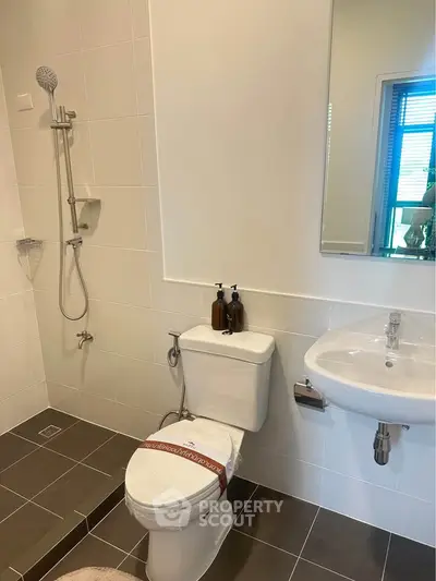 Modern bathroom with sleek fixtures and neutral tiles, featuring a shower and toilet.