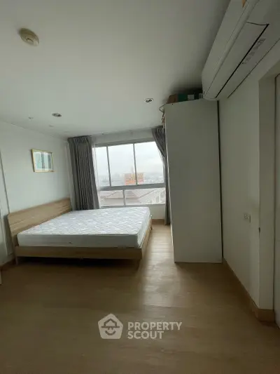 Spacious bedroom with large window offering city views, featuring a comfortable bed and ample natural light.