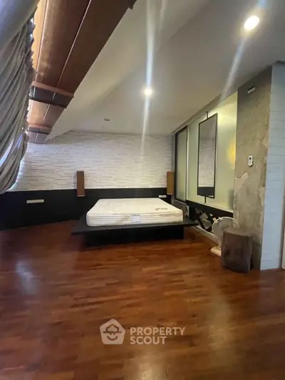Spacious bedroom with modern design and wooden flooring, featuring a minimalist bed setup.