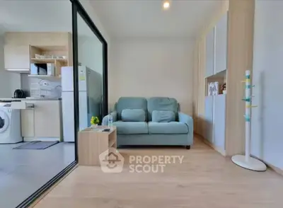 Modern living room with open kitchen, featuring a cozy sofa and sleek appliances.
