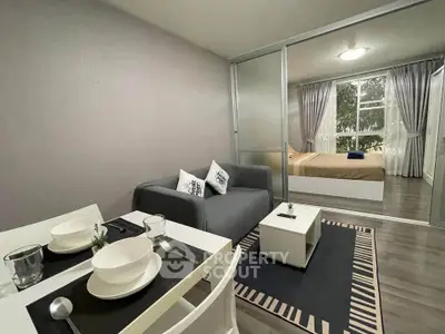 Modern open-plan living room with dining area and bedroom, featuring sleek furniture and large windows.