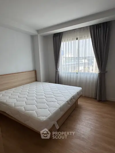 Spacious bedroom with large window and wooden flooring in modern apartment.