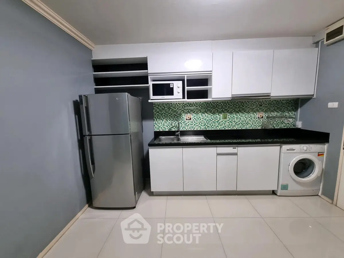 Modern kitchen with sleek cabinets, stainless steel fridge, and washing machine in stylish apartment.