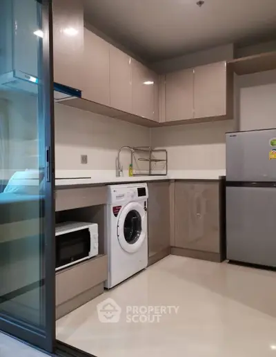 Modern kitchen with sleek cabinets, washing machine, and fridge in a compact layout.