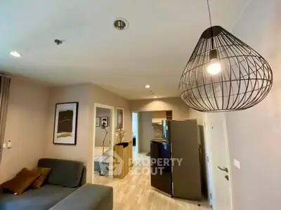 Modern living room with stylish lighting and open layout, featuring a cozy sofa and sleek kitchen appliances.