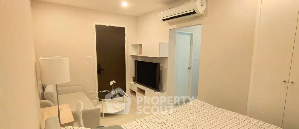 Cozy bedroom with modern decor and air conditioning, featuring a small seating area and TV unit.