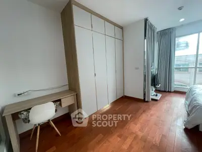 Spacious bedroom with wooden flooring, large window, and built-in wardrobe