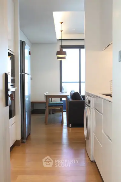 Modern kitchen with open layout and dining area, featuring sleek appliances and wooden flooring.