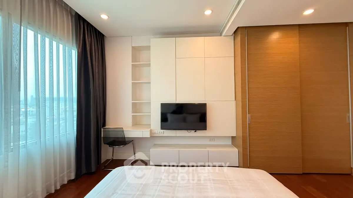 Modern bedroom with built-in storage, TV, and large window with city view.