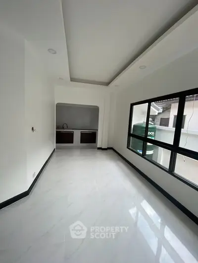 Spacious modern room with large window and sleek flooring, ideal for versatile living space.