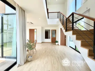 Spacious modern living room with wooden flooring, large windows, and stylish staircase in a bright open layout.