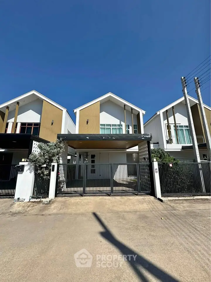 Modern townhouse with sleek design and gated entrance under clear blue sky.
