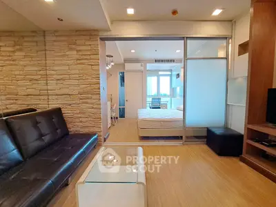 Modern condo interior with stylish living room and cozy bedroom separated by glass partition.