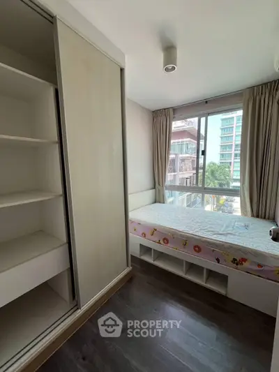 Cozy bedroom with built-in wardrobe and large window offering natural light and city view.
