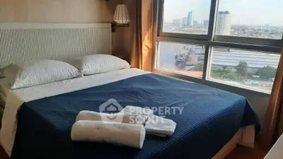 Cozy bedroom with city view, featuring a neatly made bed and large window overlooking the skyline.